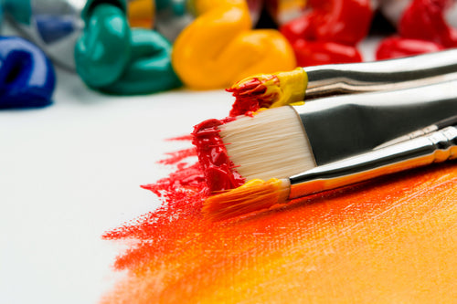 Pinceles manchados de pintura sobre un lienzo pintado de tonos cálidos.