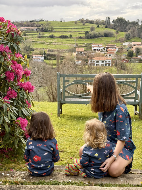 Fotografía de espaldas de madre con sus hijas. Una niña lleva el conjunto de dos piezas de pijama y la otra el mono. Conjunto Aqua Parade