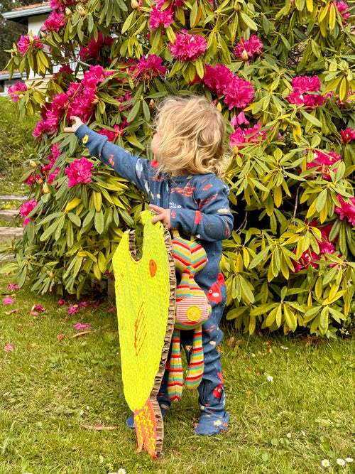 Niña llevando pijama de bebé aqua parade señalando algo y sujeta un pez de color amarillo de cartón. 